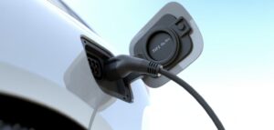 Närbild av en Typ 2-kontakt som är ansluten till en elbil. Kontakten är svart och bilen är vit. Bilden är tagen i dagsljus.